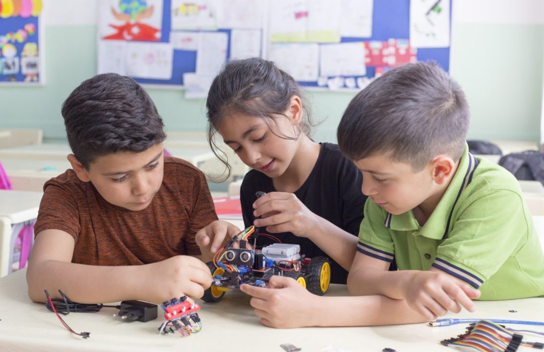 Tres estudiantes manipulando un pequeño robot de tecnología educativa | Getty Images